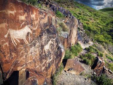 Ancient Petroglyph Of Goats And People On The Stone In Open Air Museum, Tanbaly, Kazakhstan